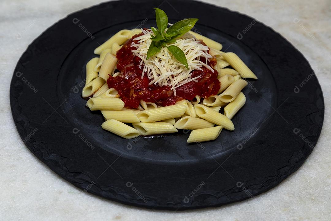 Massa penne com molho vermelho e queijo parmesão em um prato preto