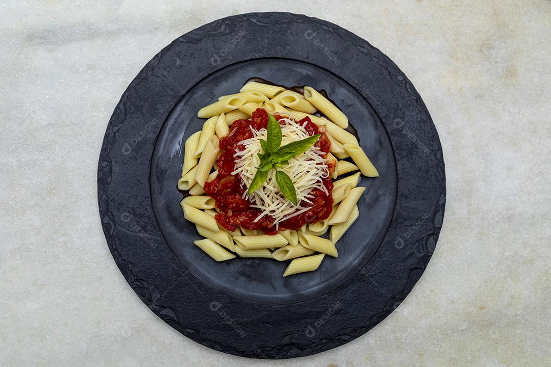 Massa penne com molho vermelho e queijo parmesão em um prato preto