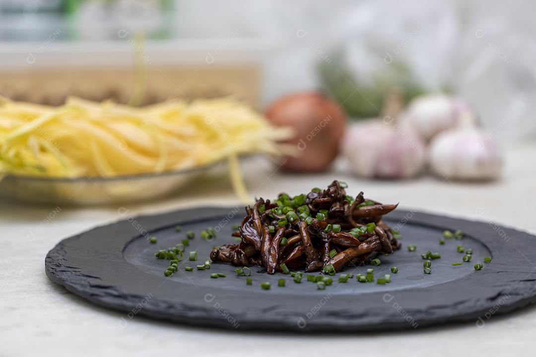 Cogumelo Shimeji servido com cebolinha no prato de pedra preta. Tipica JPG