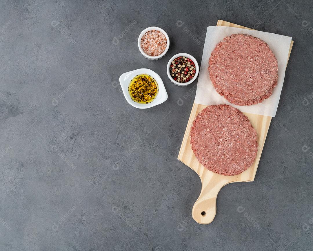 Hambúrguer de carne crua sobre placa de madeira com temperos