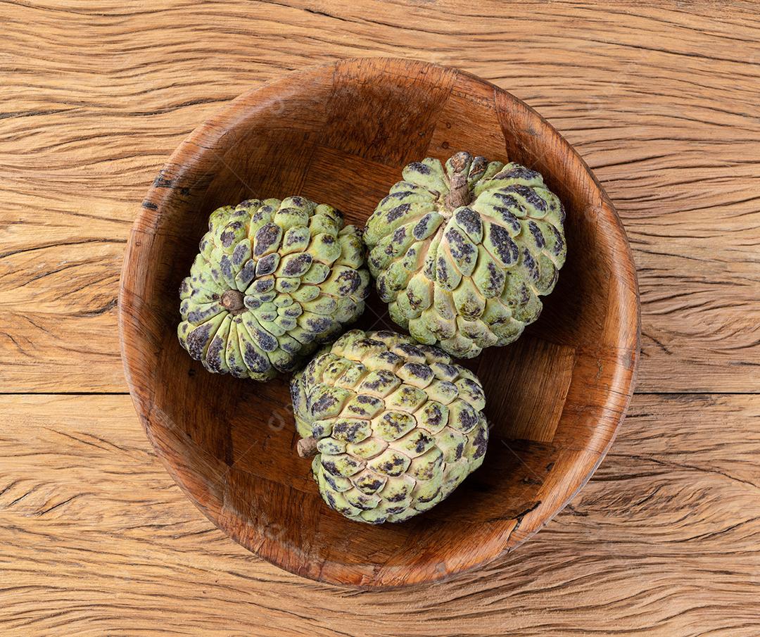 Maçãs de açúcar ou pinha em uma tigela sobre a mesa de madeira.