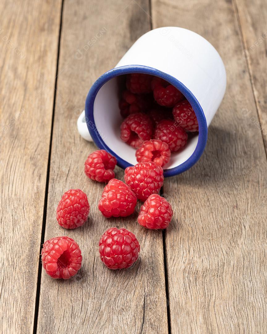 Um grupo de framboesas em um copo sobre mesa de madeira JPG