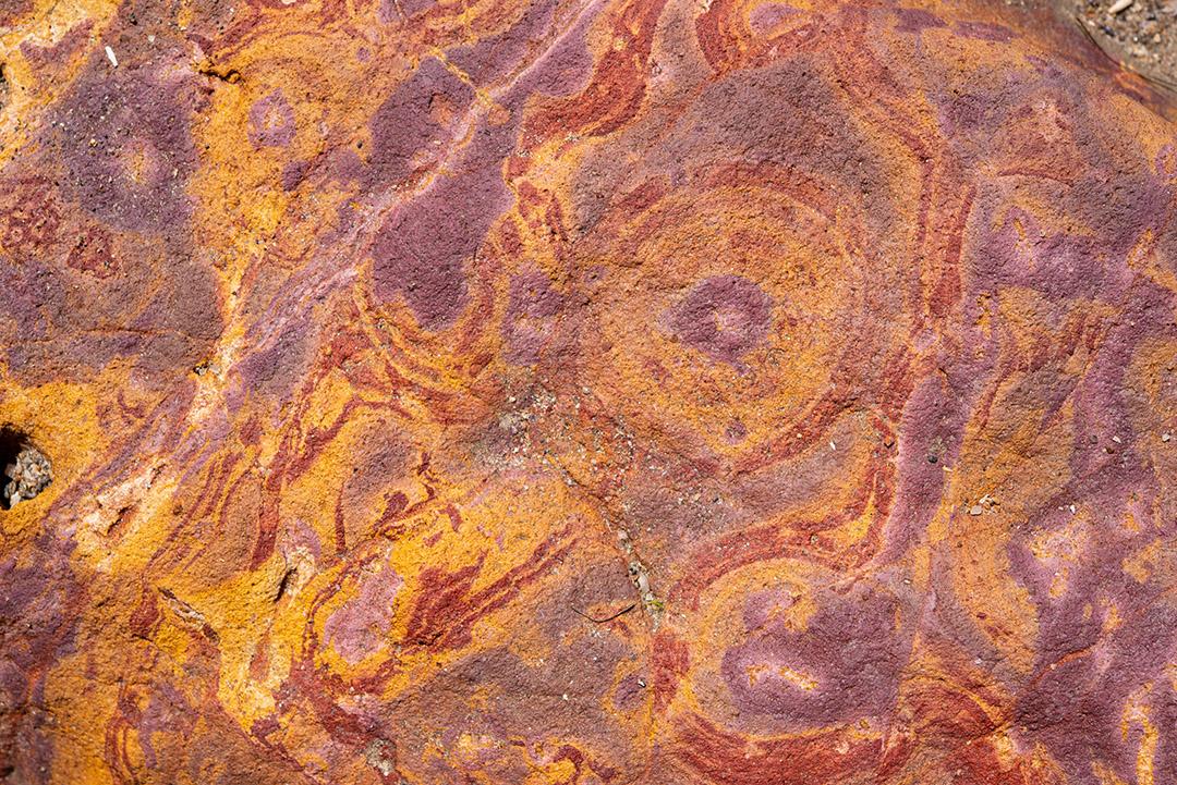 Areia colorida e rochas sedimentares, criando padrões abstratos na praia