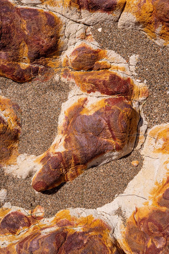 Areia colorida e rochas sedimentares, criando padrões abstratos na praia