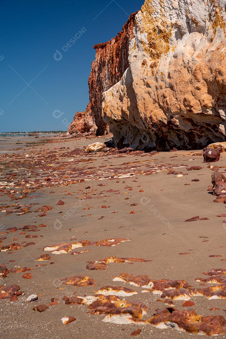 Areia colorida e rochas sedimentares, criando padrões abstratos na praia