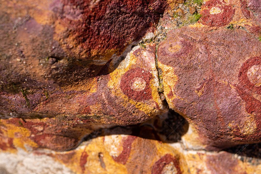 Areia colorida e rochas sedimentares, criando padrões abstratos na praia