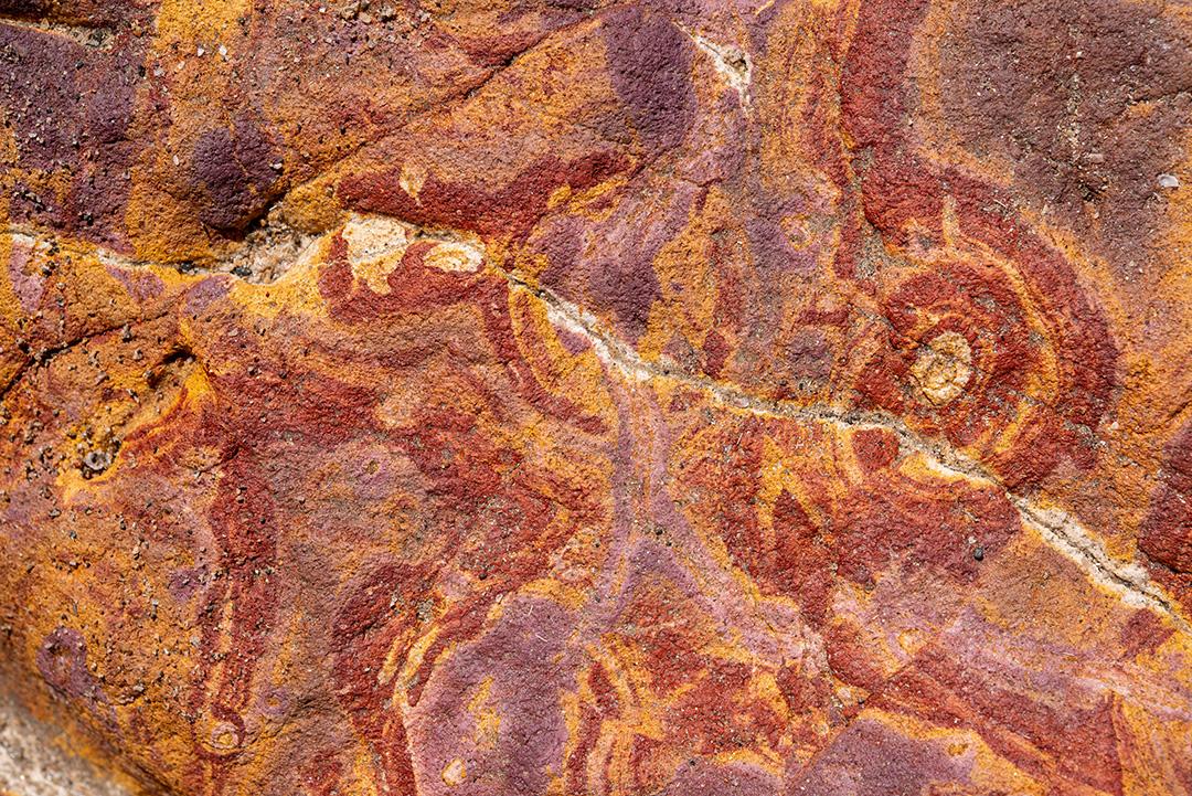 Areia colorida e rochas sedimentares, criando padrões abstratos na praia