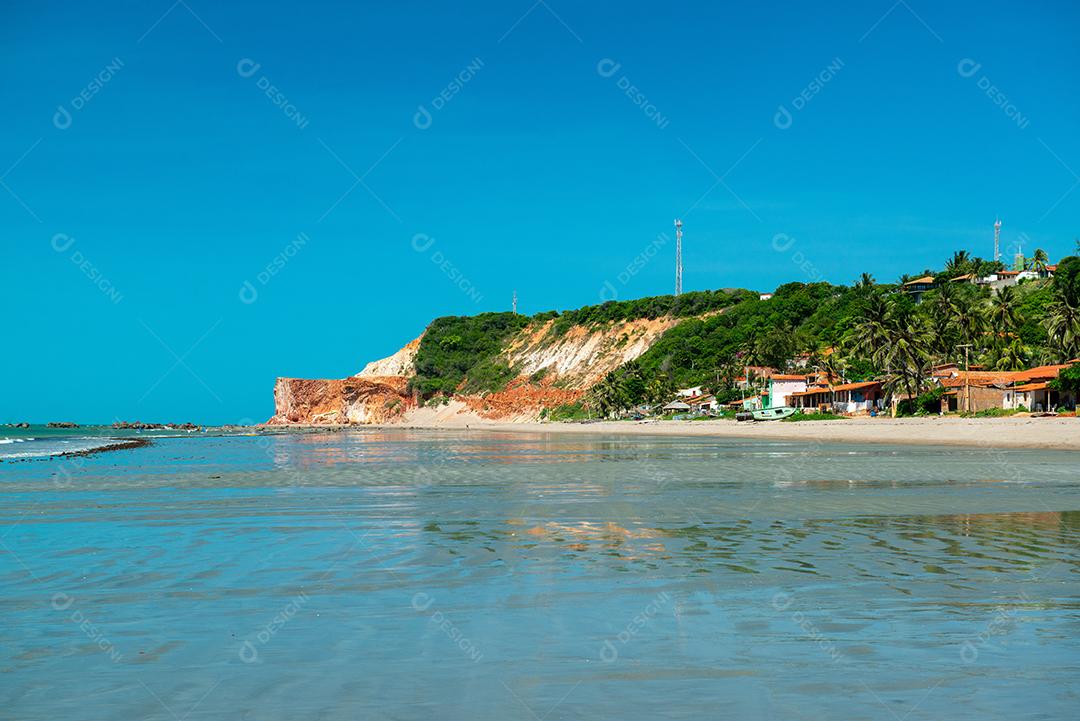 Manhã ensolarada, onde você pode ver barcos, casas e a falésia com vegetação ao fundo na Praia Redonda