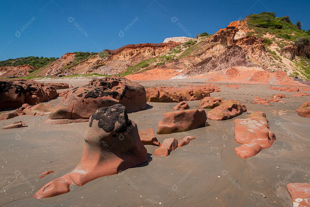 Pedras coloridas e areia na praia, ao fundo falésias com vegetação natural na Praia de Peroba