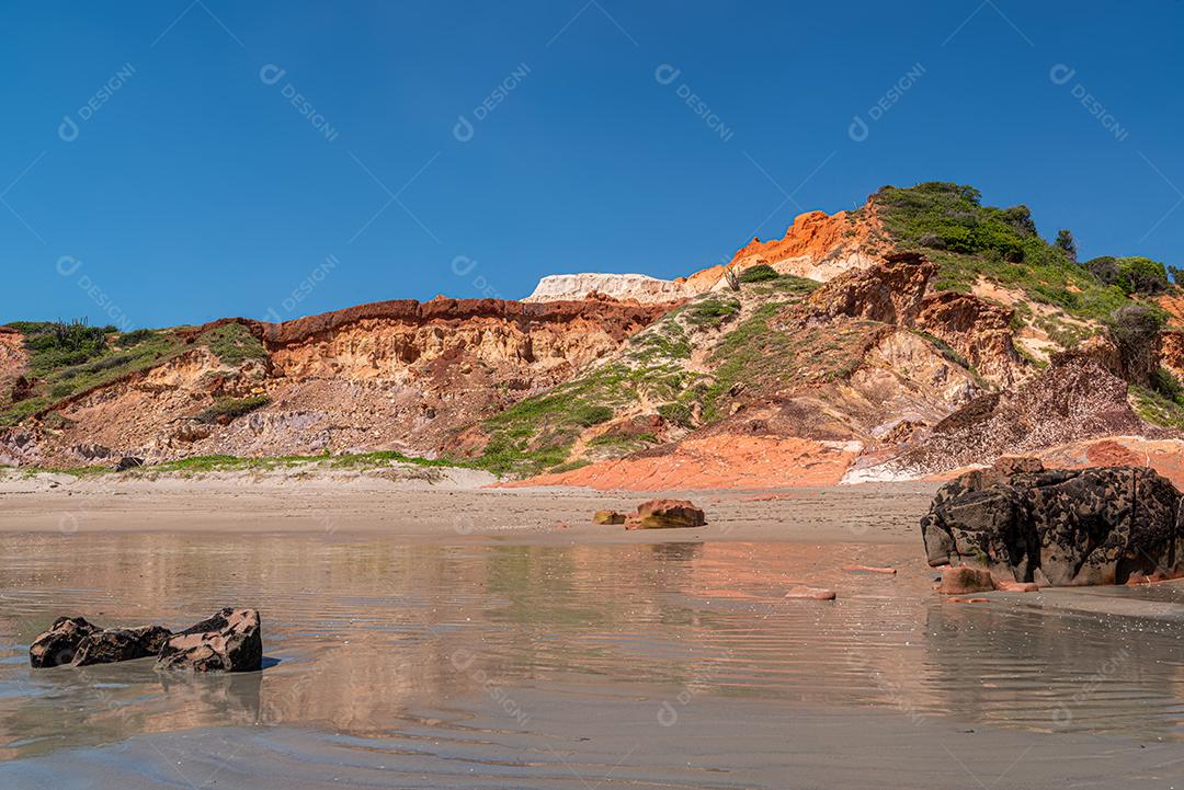 Pedras coloridas e areia na praia, ao fundo falésias com vegetação natural na Praia de Peroba