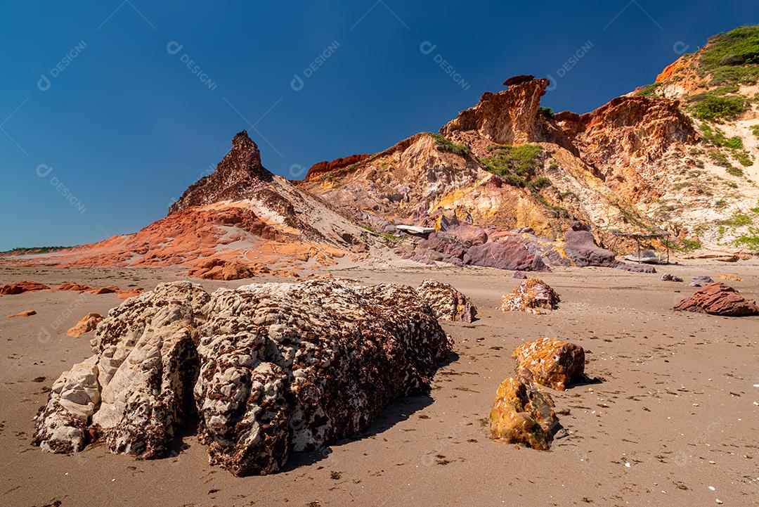 Pedras coloridas e areia na praia, ao fundo falésias com vegetação natural na Praia de Peroba