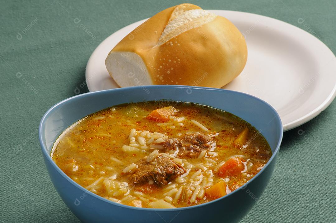 Sopa de carne com arroz legumes tigela de plástico azul acompanhada de pão prato branco
