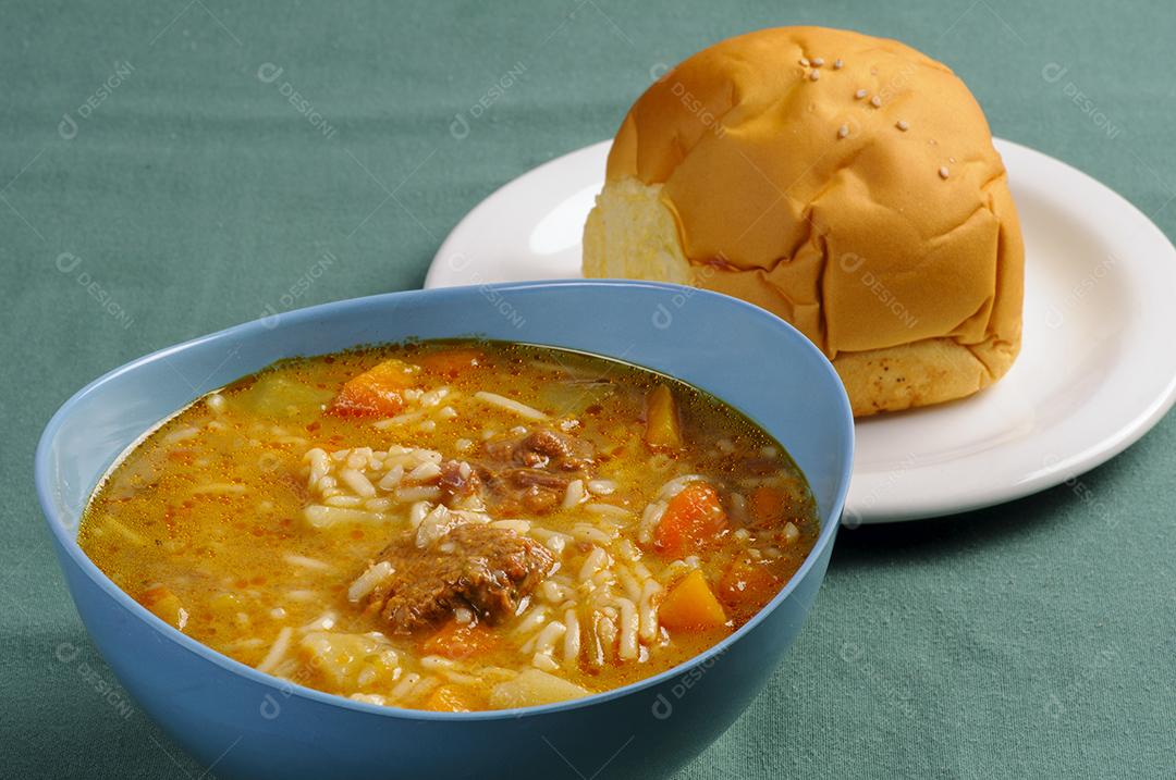 Sopa de carne com arroz legumes tigela de plástico azul acompanhada de pão prato branco