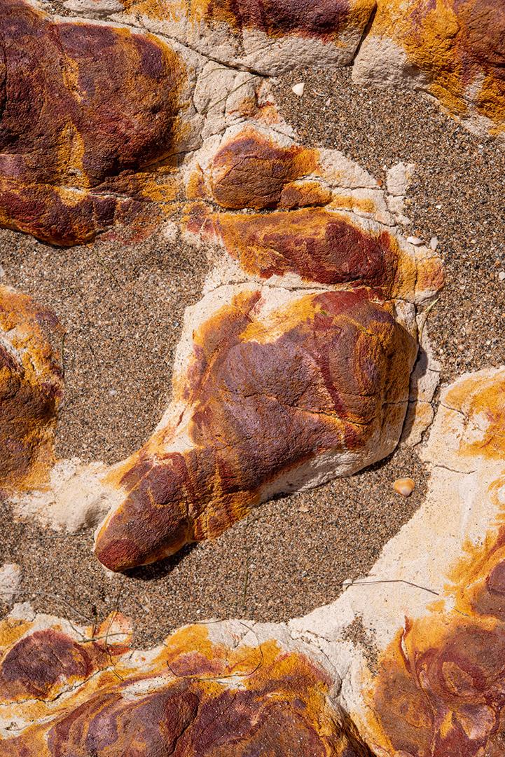 Areia colorida e rochas sedimentares, criando padrões abstratos na praia de Peroba