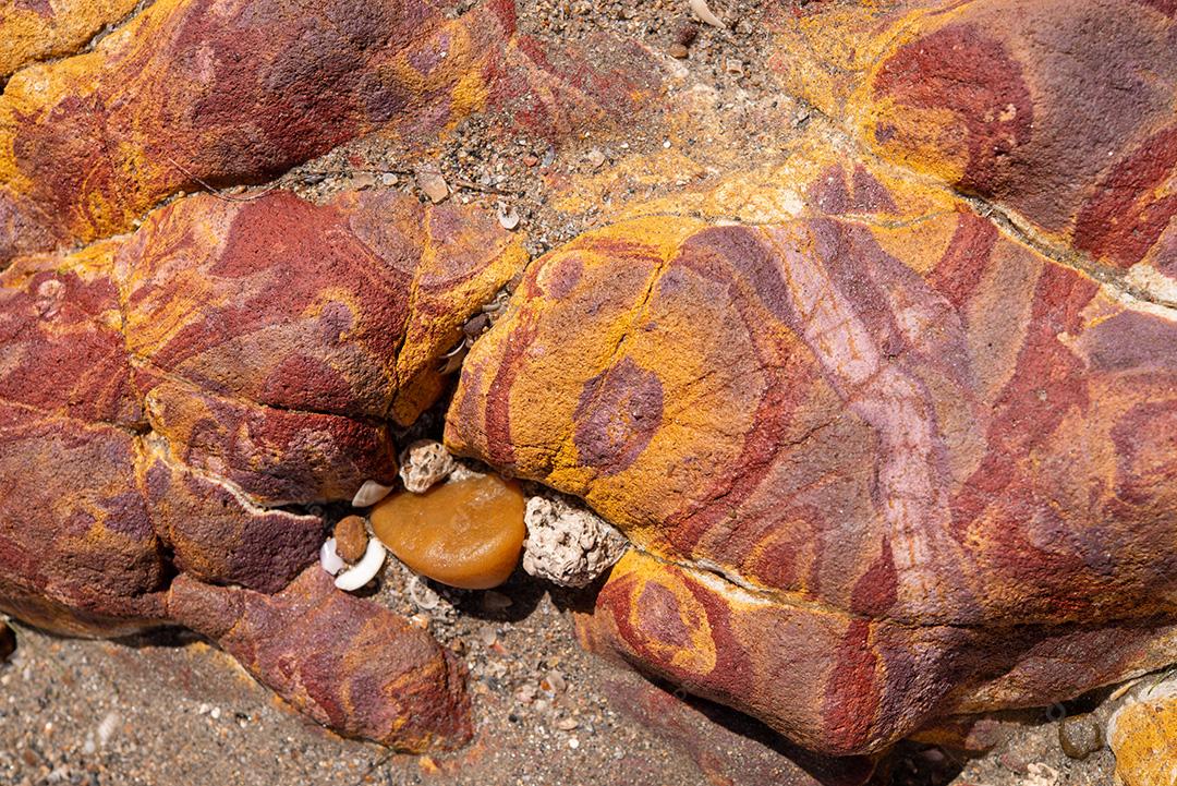 Areia colorida e rochas sedimentares, criando padrões abstratos na praia de Peroba