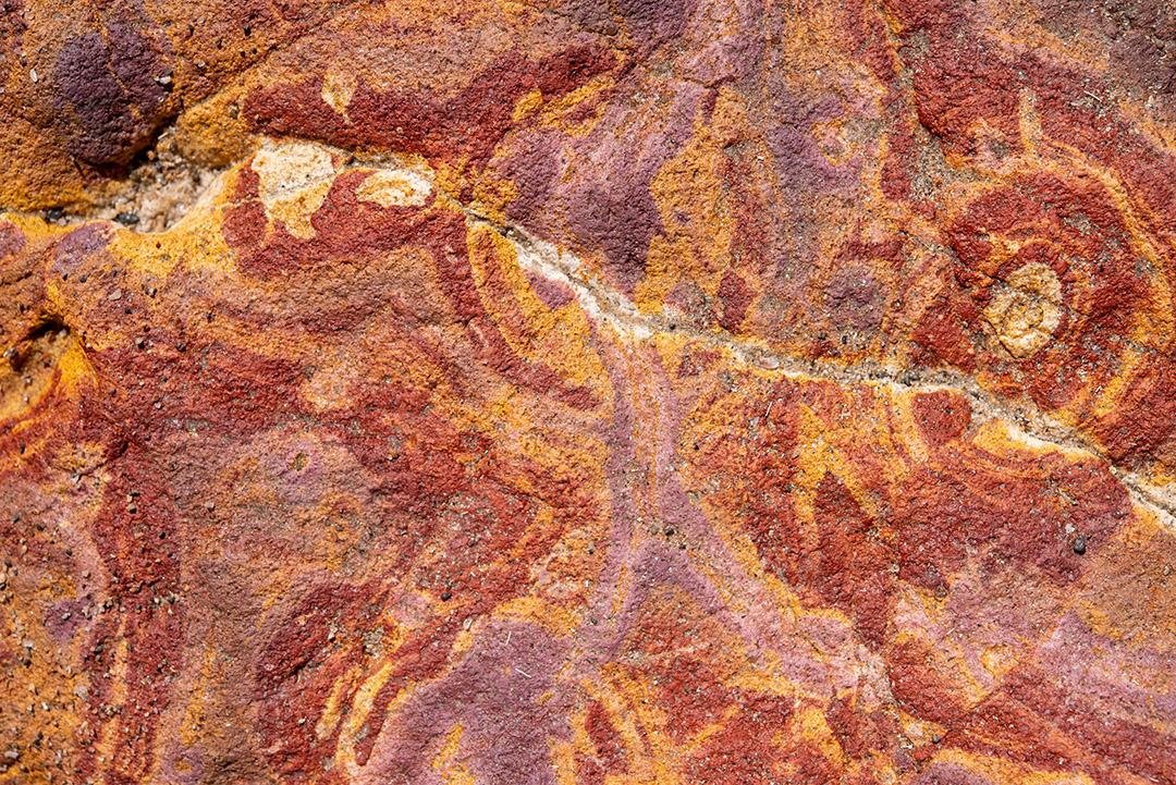 Areia colorida e rochas sedimentares, criando padrões abstratos na praia de Peroba