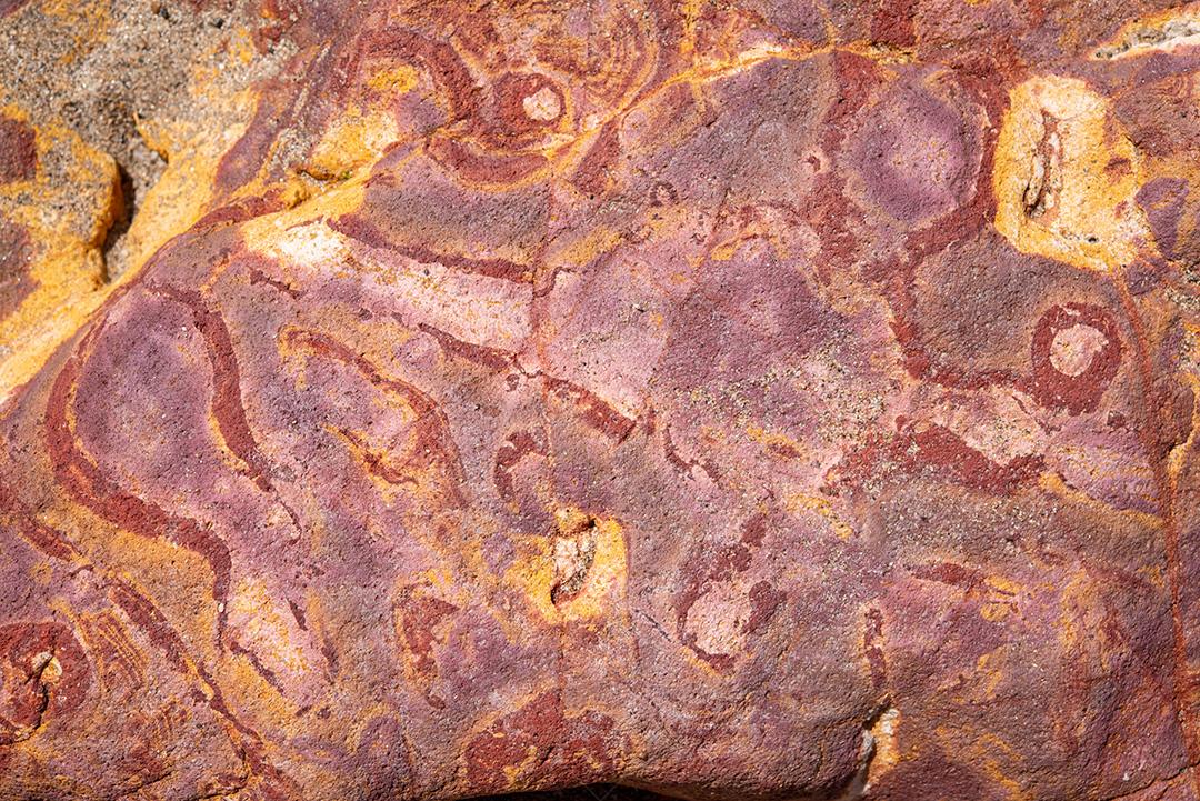 Areia colorida e rochas sedimentares, criando padrões abstratos na praia de Peroba