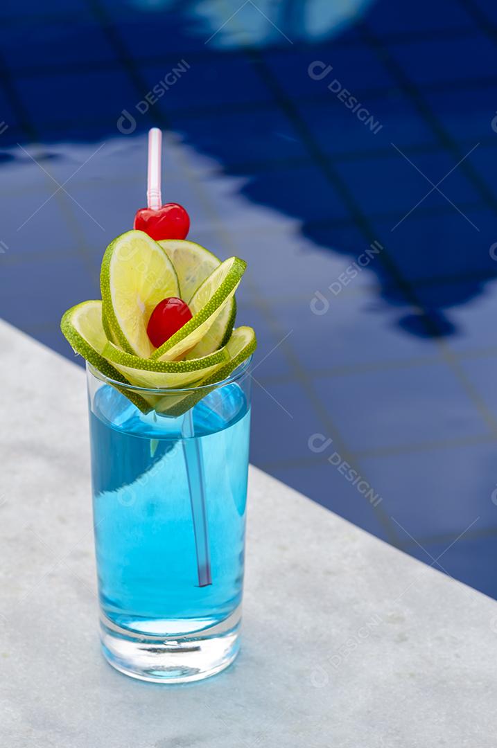 Bebida azul com limão e cerejas à beira da piscina com fundo desfocado