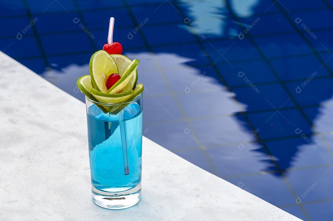 Bebida azul com limão e cerejas à beira da piscina com fundo desfocado