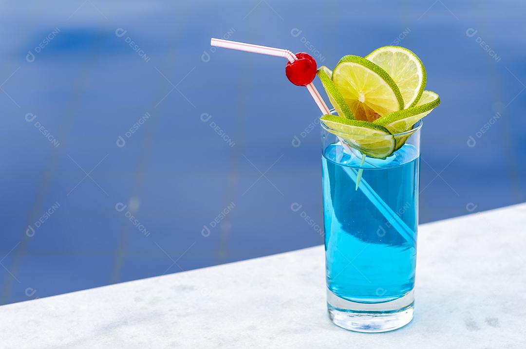 Bebida azul com limão e cerejas à beira da piscina com fundo desfocado