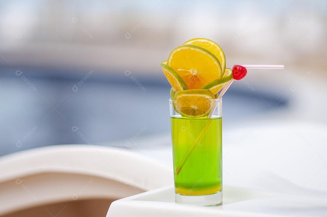 Bebida verde com laranja e cerejas à beira da piscina com fundo desfocado