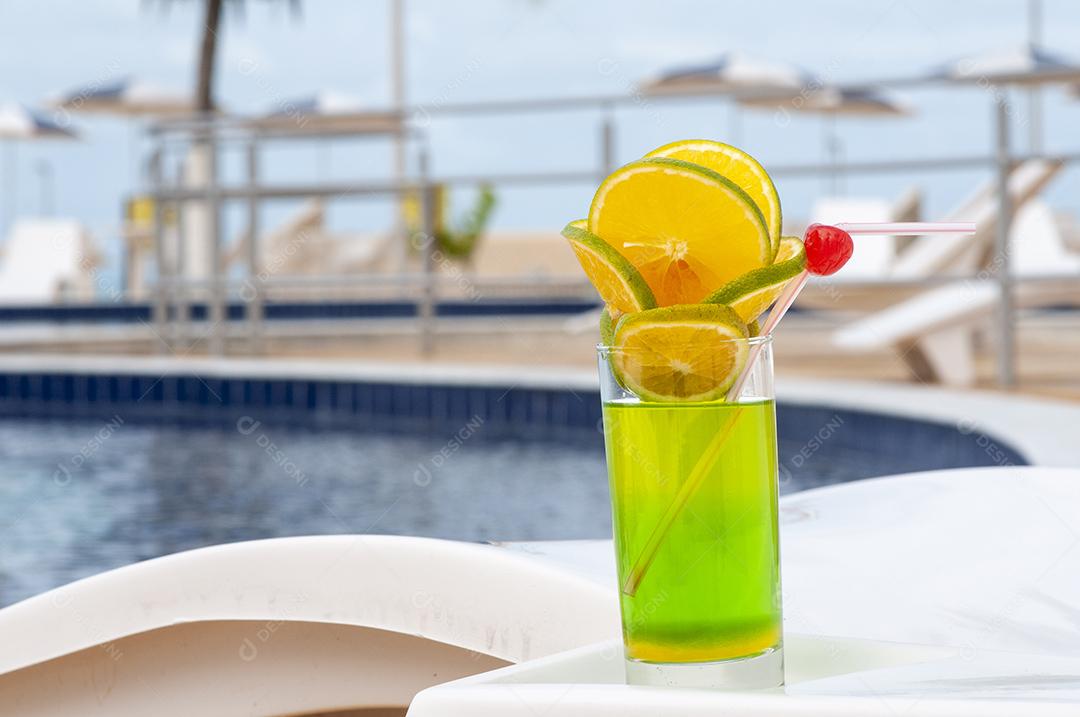Bebida verde com laranja e cerejas à beira da piscina com fundo desfocado