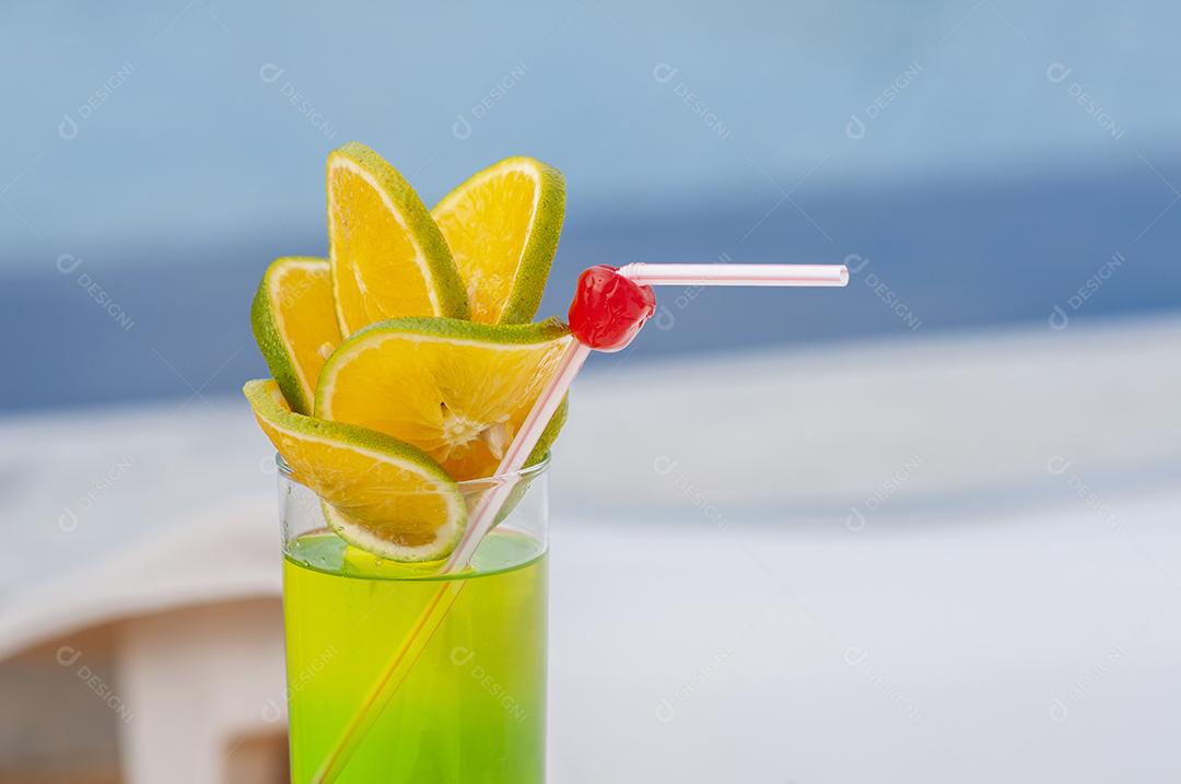 Bebida verde com laranja e cerejas à beira da piscina com fundo desfocado