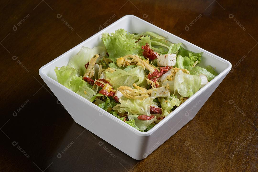 Salada verde com camarão em tigela branca na mesa de madeira.