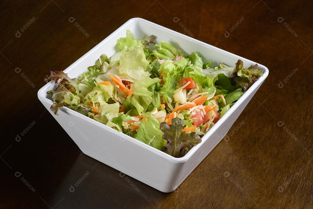 Salada verde com camarão em tigela branca na mesa de madeira.