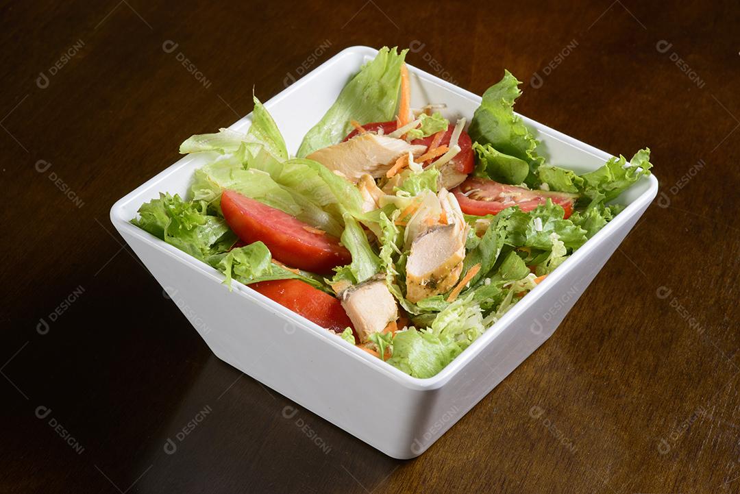 Salada verde com camarão em tigela branca na mesa de madeira.