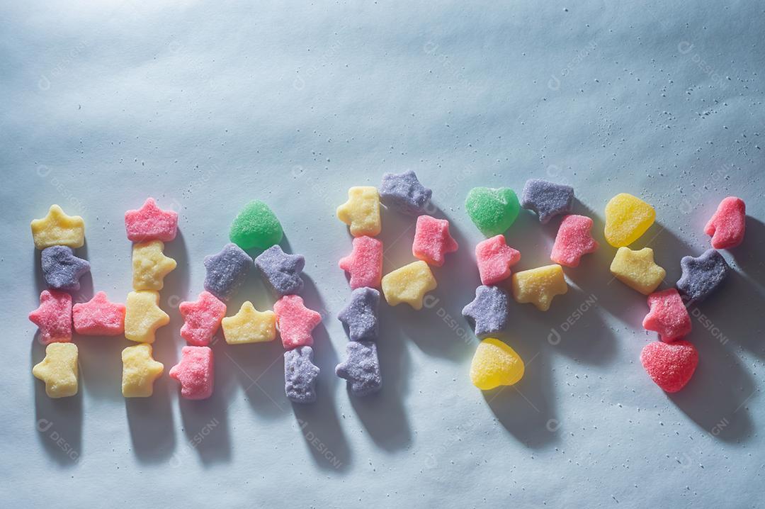 Doces coloridos variavam com a palavra Feliz escrita, fundo azul claro