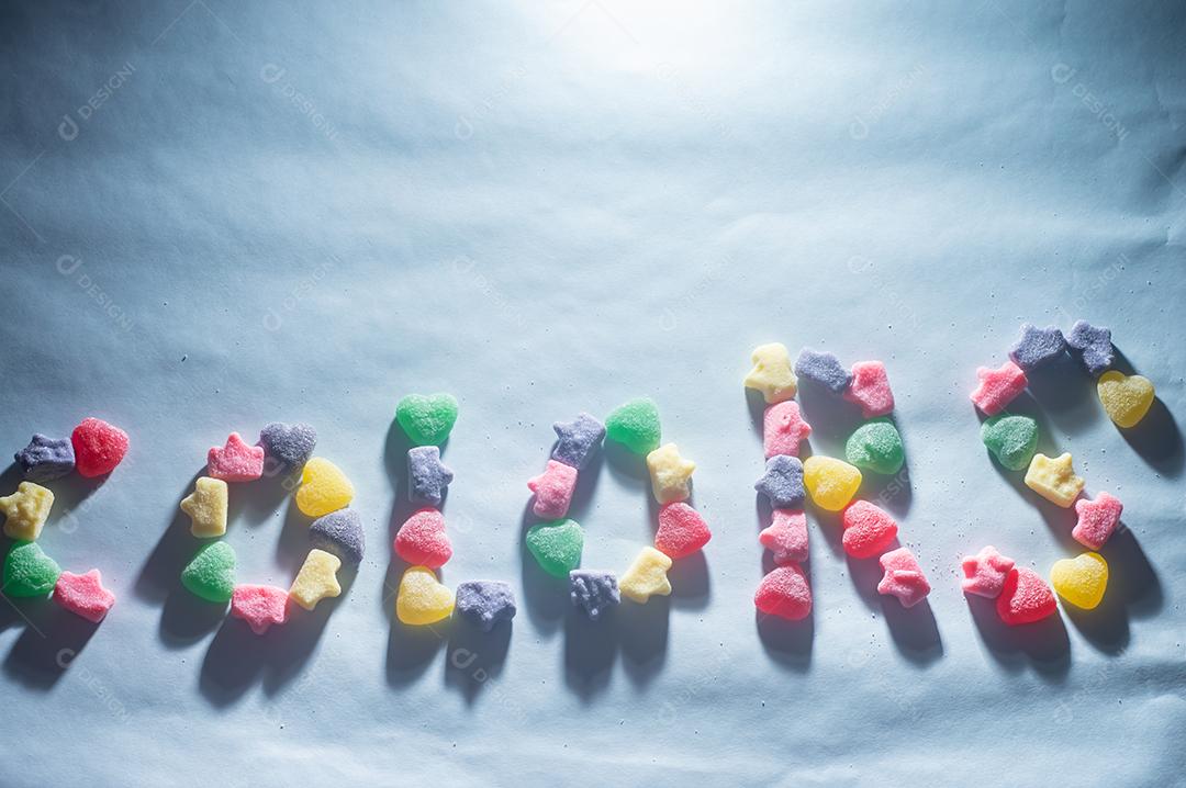 Doces coloridos variados com a palavra colors escrita, fundo azul claro