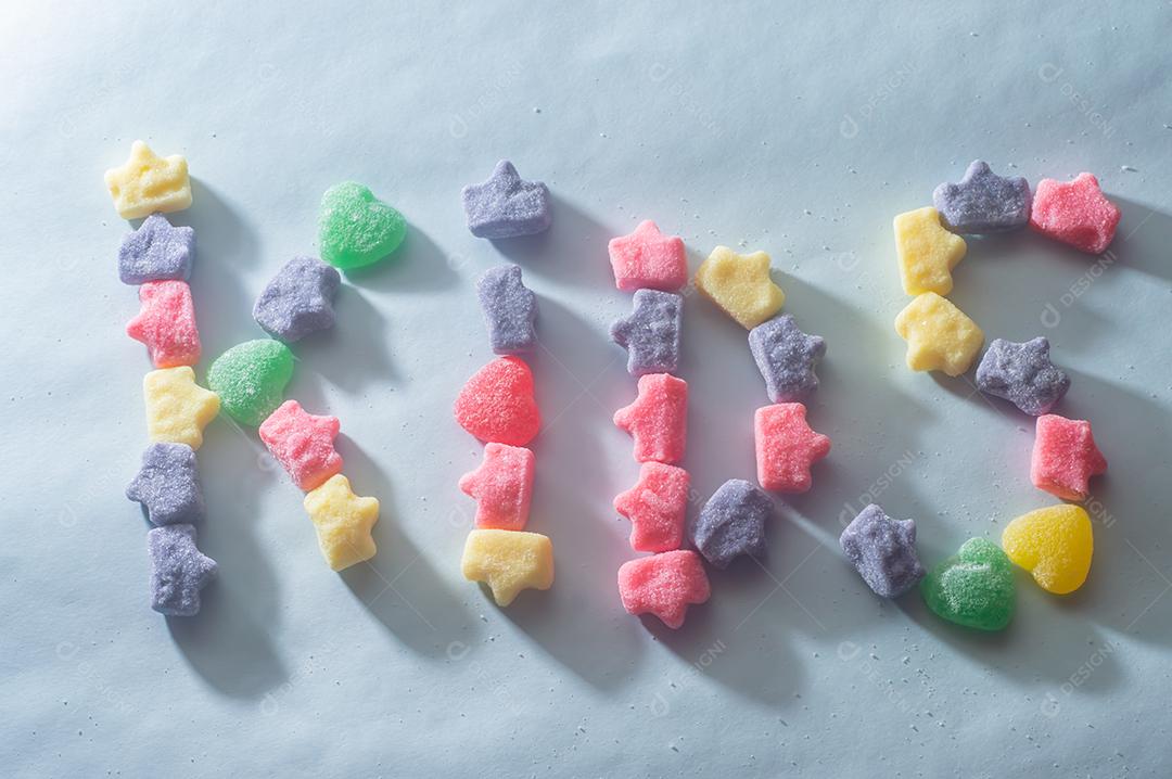 Doces coloridos variados com a palavra kids escrita, fundo azul claro