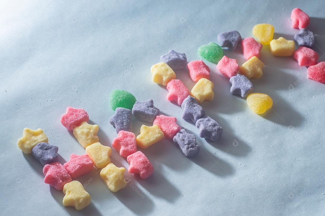 Doces coloridos variados com a palavra Happy escrita, fundo azul claro