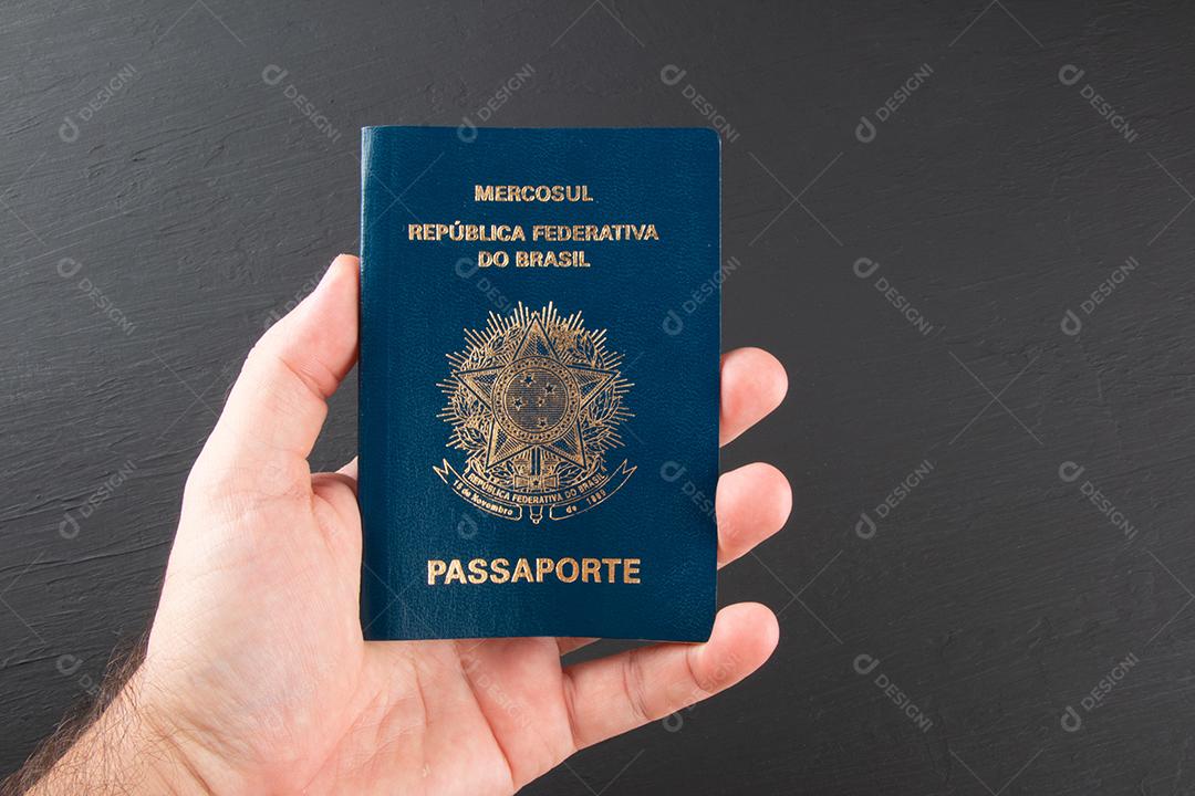 Mão segurando passaporte brasileiro com fundo preto