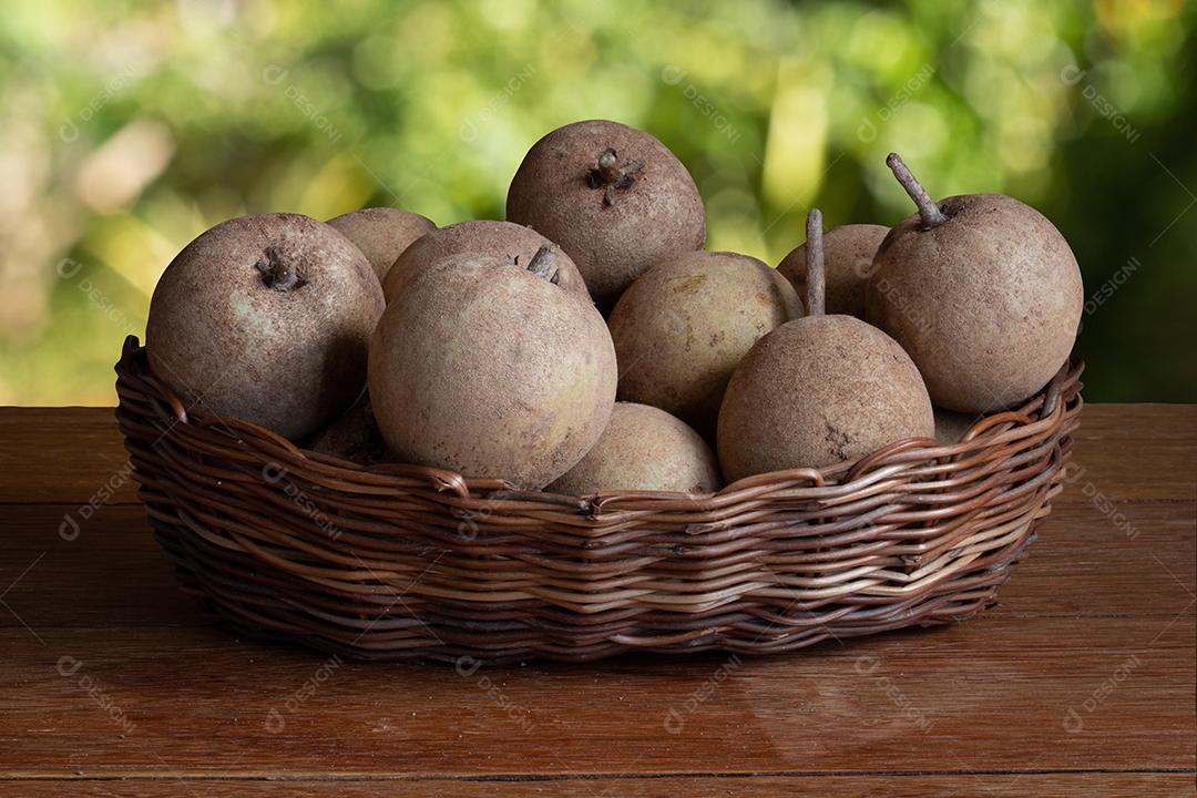Sapodillas fruta exposta em cesta sobre mesa e fundo verde