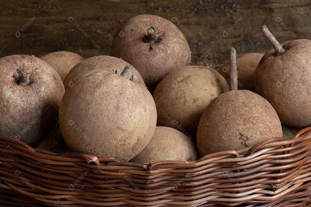 Fruta sapotis exposta em cesta em fundo de madeira rústica