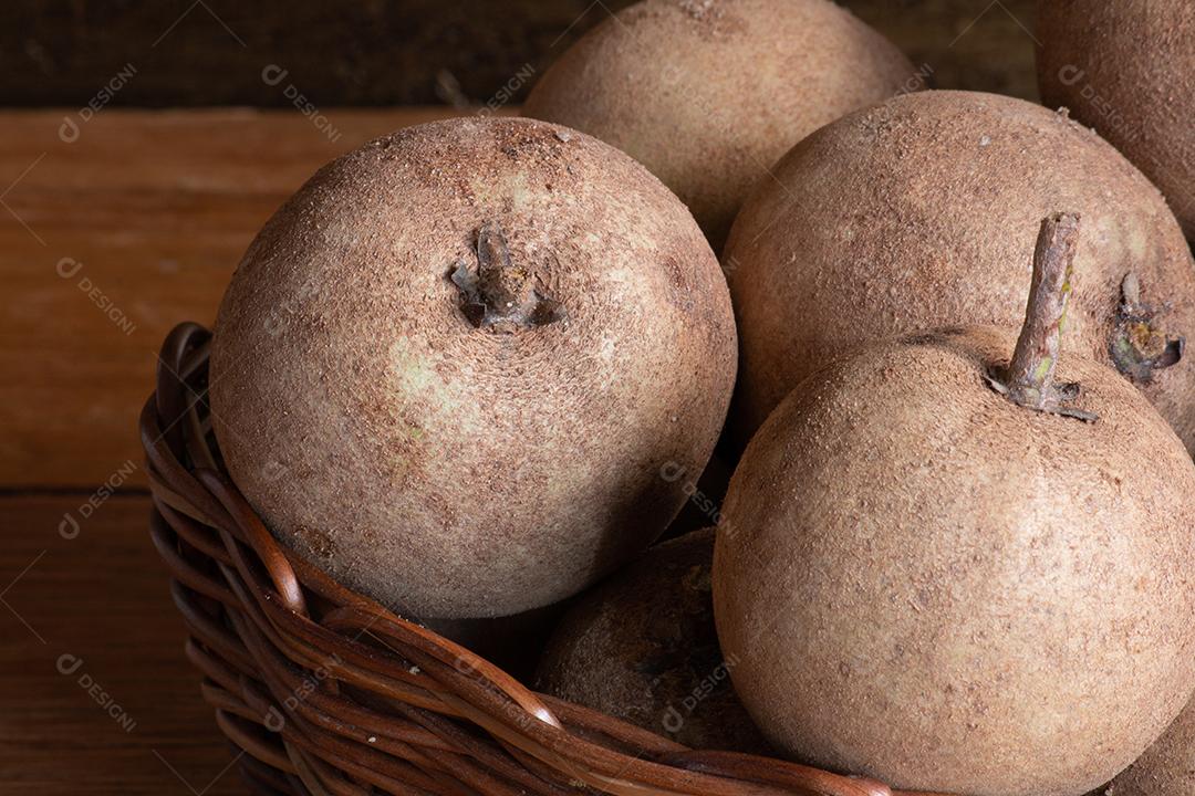Fruta sapotis exposta em cesta em fundo de madeira rústica