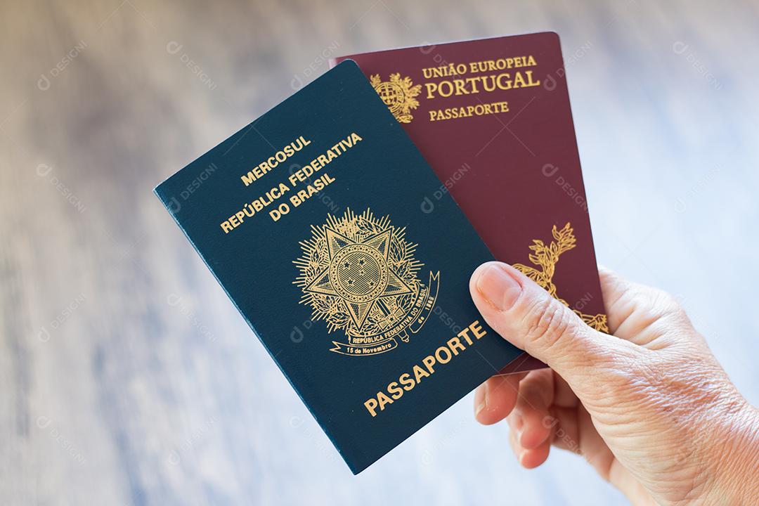 Mão segurando passaporte português e passaporte brasileiro