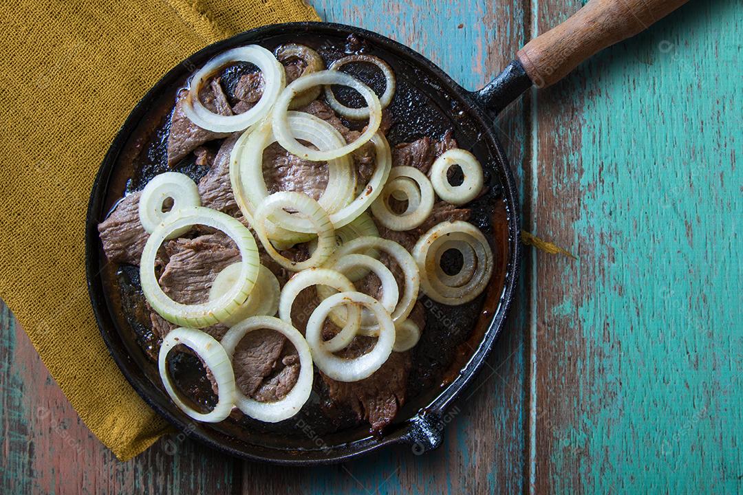 Carne frita no prato de ferro com cebola com fundo de madeira envelhecida