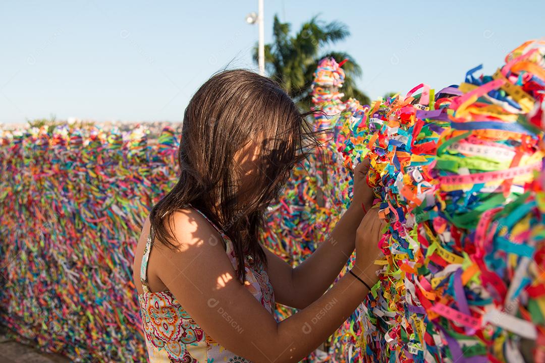 Garota fazendo pedidos e amarrando fitas coloridas na grade