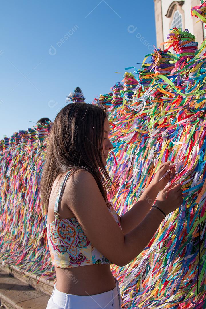 Garota fazendo pedidos e amarrando fitas coloridas na grade