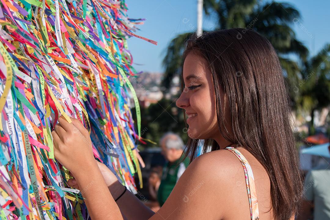 Garota fazendo pedidos e amarrando fitas coloridas na grade