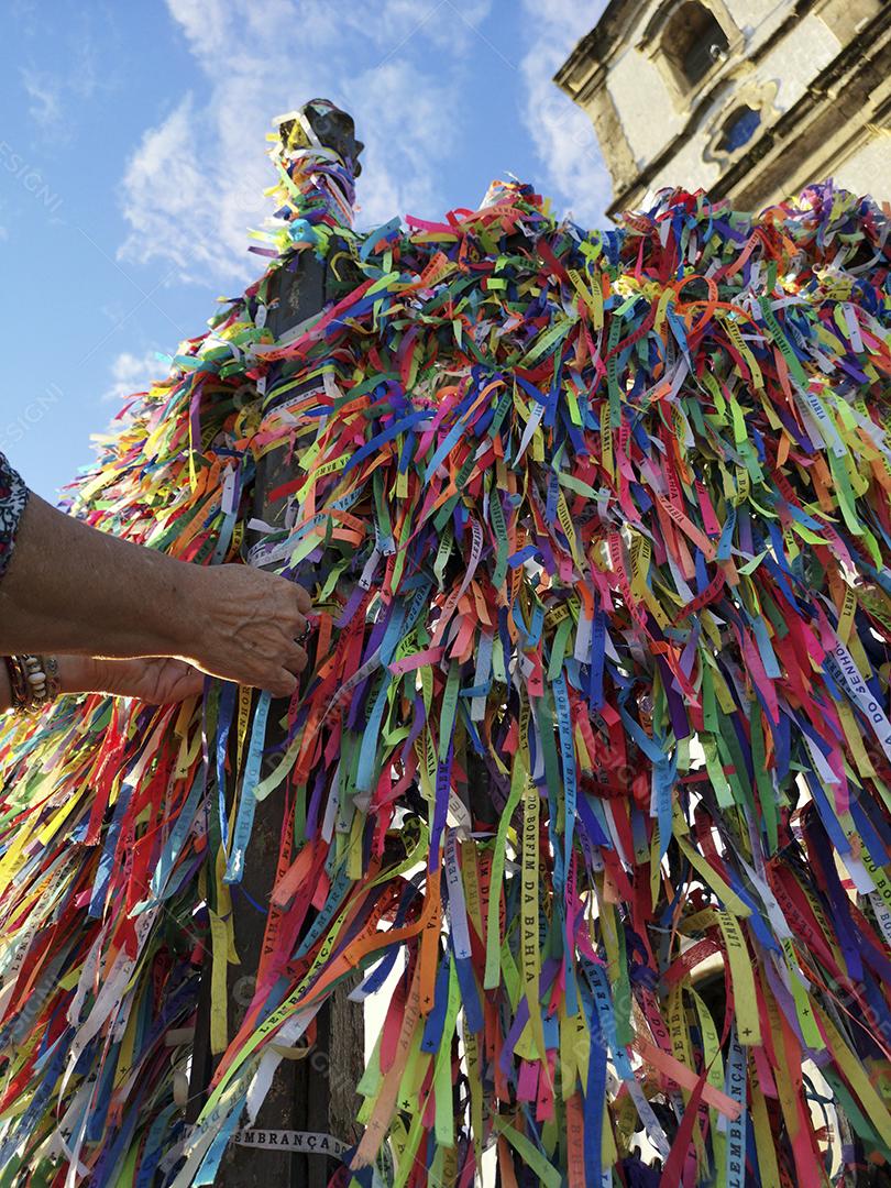 Mãos femininas amarrando fitas coloridas na grade da igreja do Bonfim