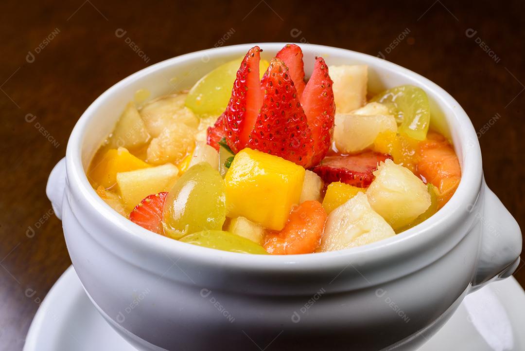 Salada de frutas com morango, uva verde, manga e abacaxi Servido em uma tigela branca.