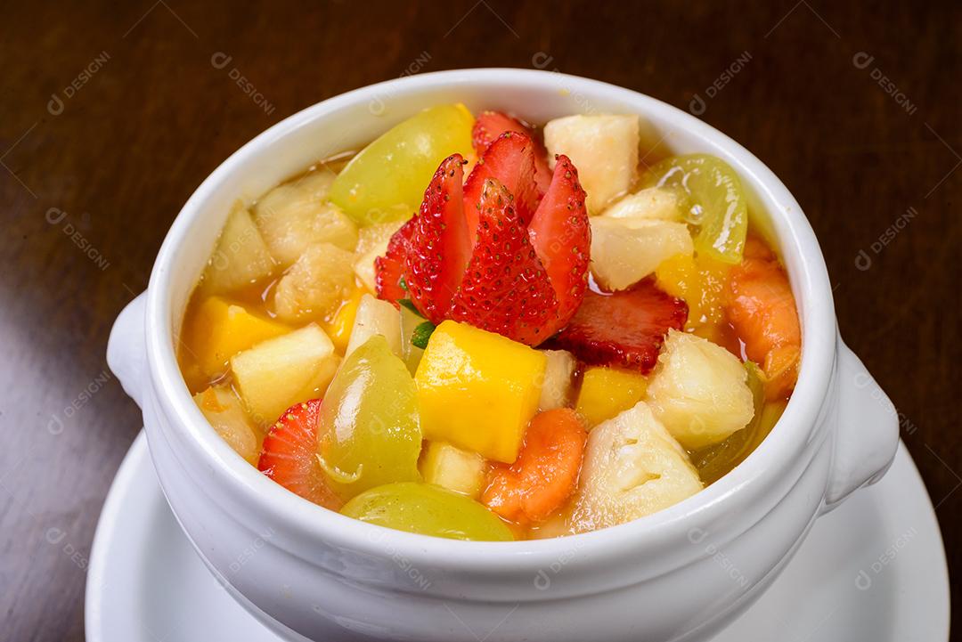 Salada de frutas com morango, uva verde, manga e abacaxi Servido em uma tigela branca.