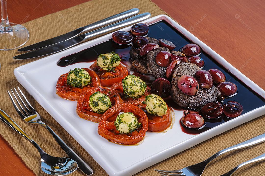 Filet mignon ao molho de uva, acompanhado de campeões e tomates servidos à mesa.