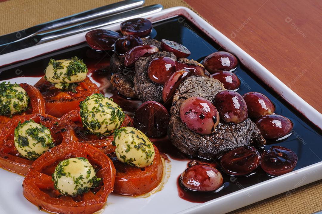 Filet mignon ao molho de uva, acompanhado de campeões e tomates servidos à mesa.