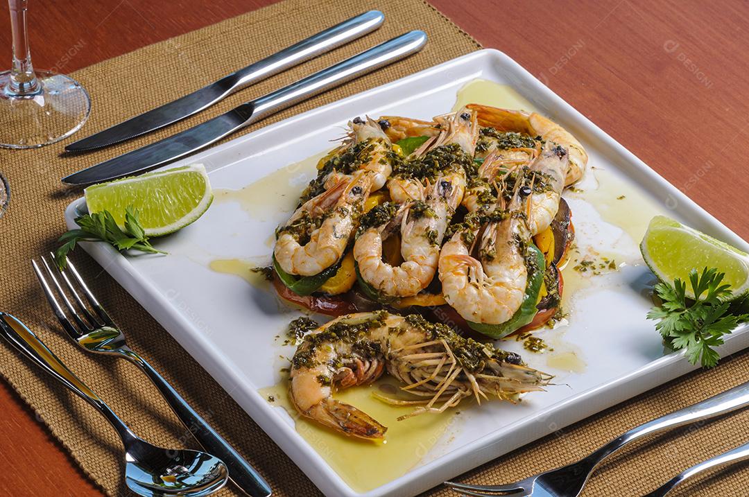 Camarões com legumes salteados em azeite, num prato quadrado branco servido à mesa.