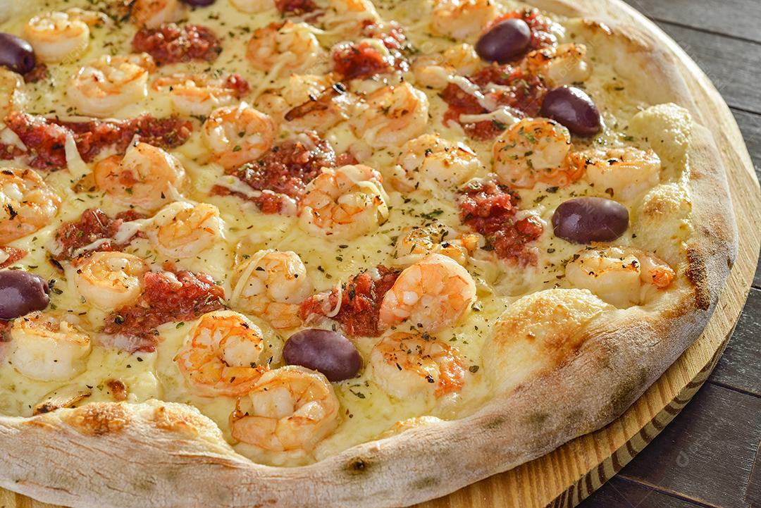 Pizza de camarão com azeitonas em close-up de pá de madeira.